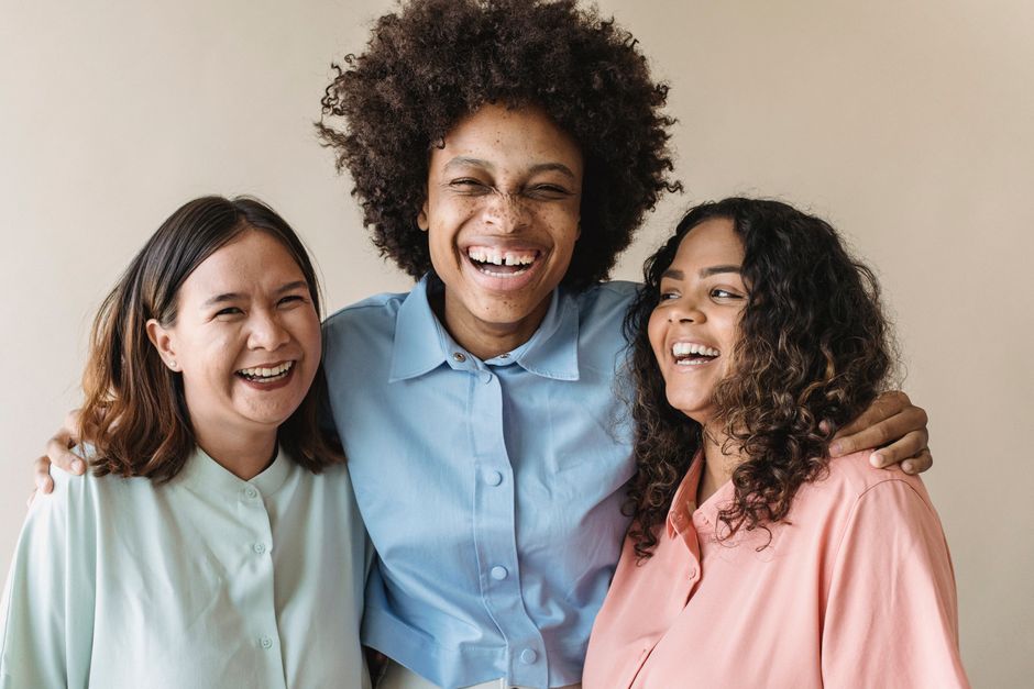 Ação Comunitária. — Three women of diverse backgrounds sharing a joyful moment, showcasing happiness and unity.