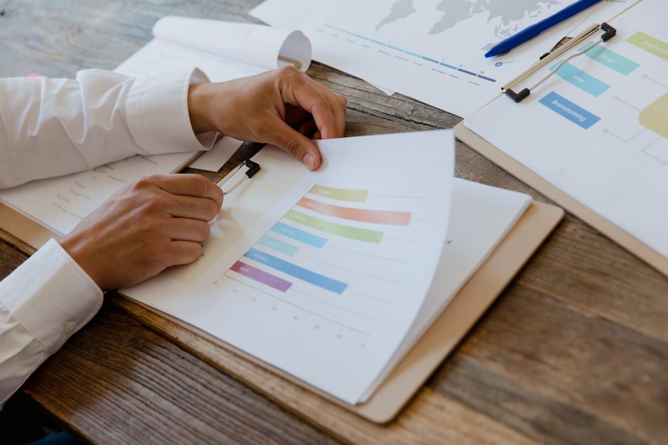 Ação Comunitária. — Close-up of hands reviewing business report with colorful charts and graphs on a wooden desk.